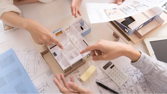間取り模型や図面を囲んで住宅設計の打ち合わせをする複数人の手元